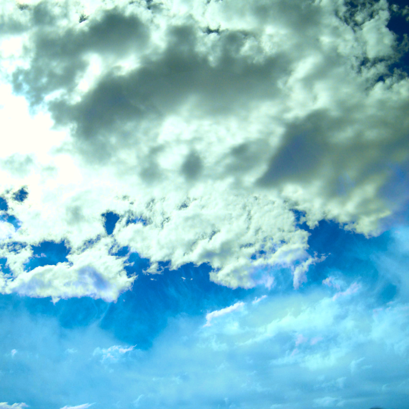 A blue sky with bright, voluminous clouds in the top portion and wispy cirrus clouds in the bottom.